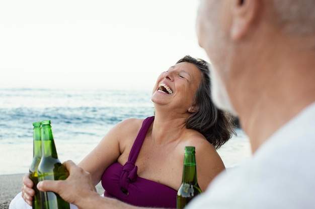 Senior man and woman laughing on the beach while having beer