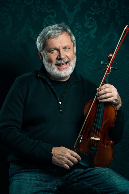 Free Photo senior musician playing a violin with a wand on black studio