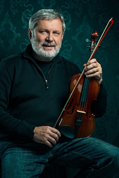 Senior musician playing a violin with wand on black wall