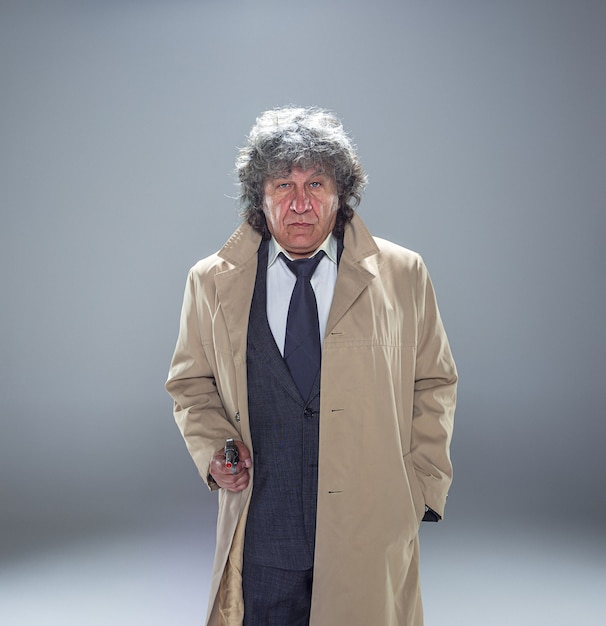 Free photo senior police agent with a gun standing as detective or mafia boss. studio shot on gray in retro stile