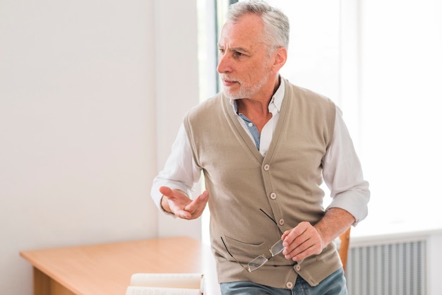 Free photo senior professor explaining lesson near desk in classroom