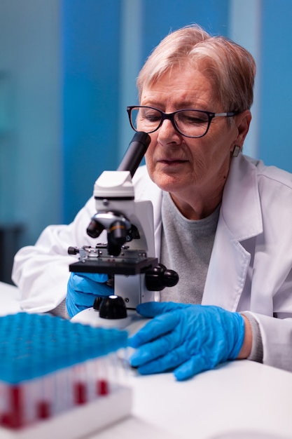 Senior scientist looking through microscope at sample in biology lab