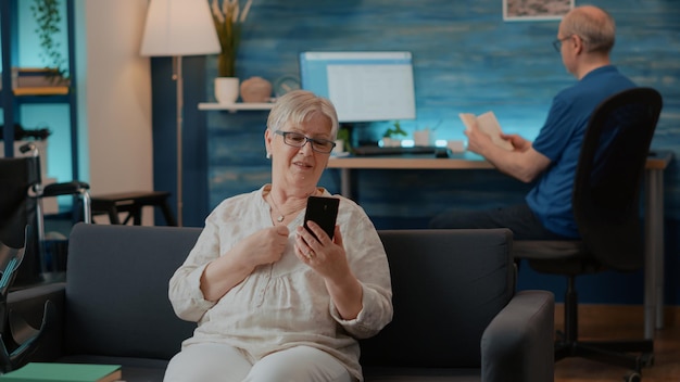 Senior woman chatting on remote video call in living room. Old adult using mobile phone to have conversation on online videoconference for telecommunication. Internet meeting on smartphone