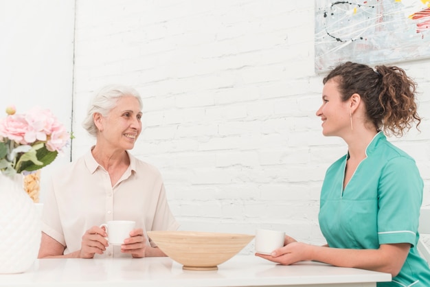 Senior woman and female nurse having coffee together