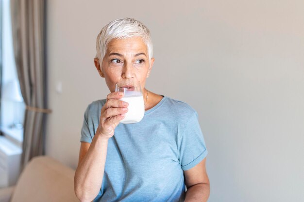 Senior Woman Holding Glass Of Milk At Home Middle age woman drinking a glass of fresh milk with a happy face standing and smiling with a confident smile showing teeth