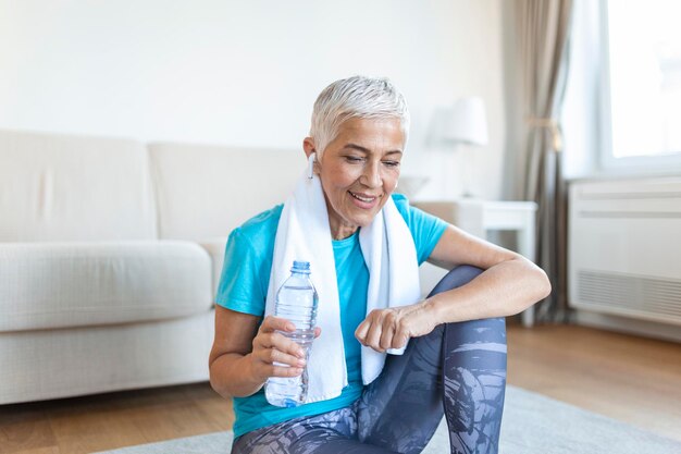 Senior woman holding plastic bottle of waterwiping sweat with a towel exhausted after the daily training