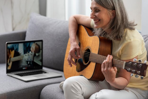 Senior woman at home on the couch using laptop for guitar lessons