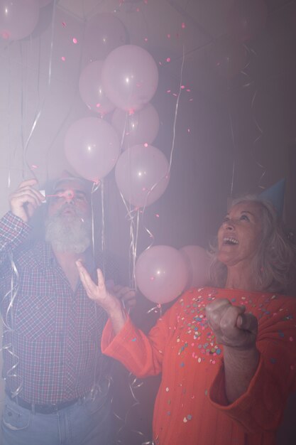 Senior woman looking at her husband blowing soap bubbles in birthday party