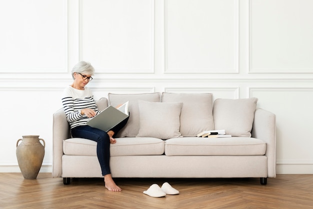 Free photo senior woman reading a book on the sofa in a scandinavian decor living room