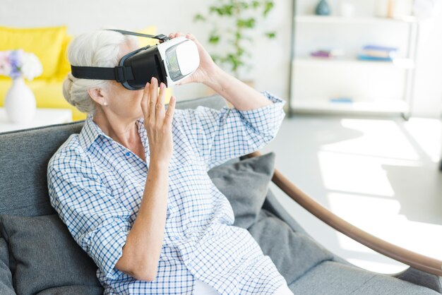 Senior woman sitting on sofa wearing virtual camera