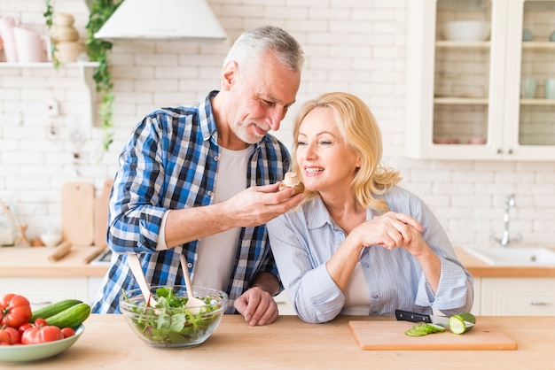 Senior woman smelling the mushroom hold by her husband in the kitchen