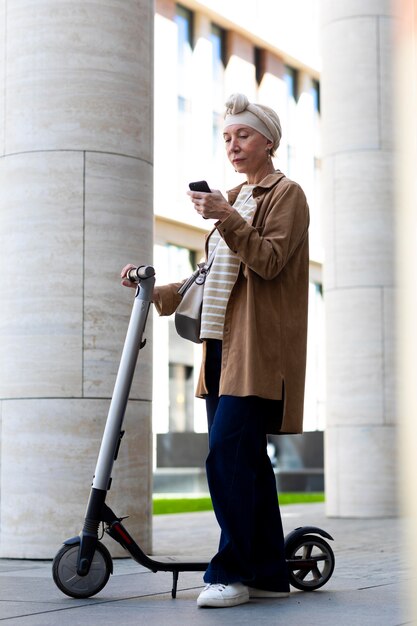 Senior woman with an electric scooter in the city using smartphone