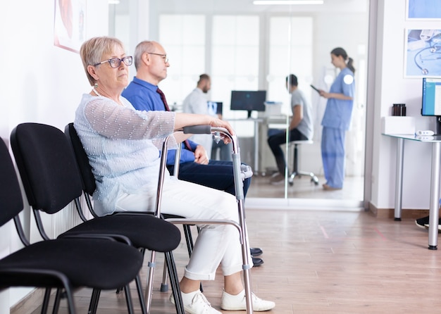 Senior woman with walking frame in hospital waiting room for rehabilitation treatment