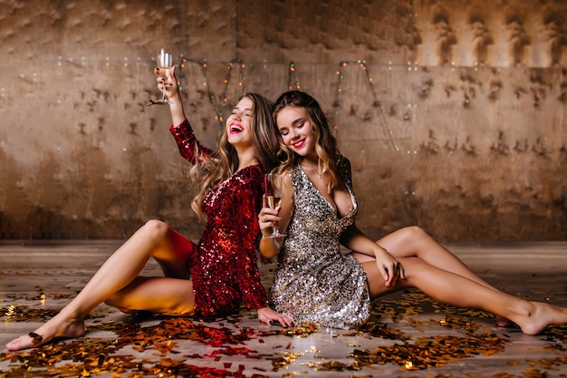 Sensual blonde woman in sparkle dress drinking champagne on the floor