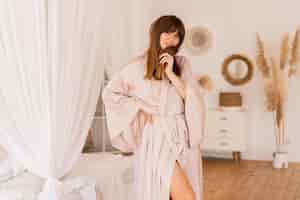 Free photo sensual brunette woman posing in beige silk kimono in  stylish light bedroom in bohoh style.