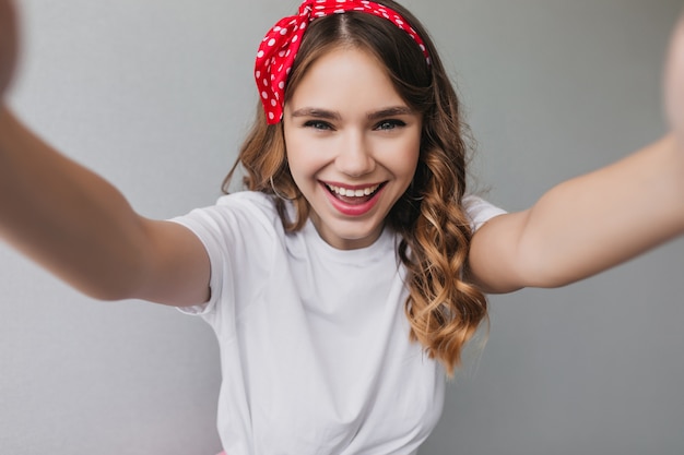 Free Photo sensual curly girl with red ribbon making selfie. indoor photo of refined female model with wavy  hairstyle laughing