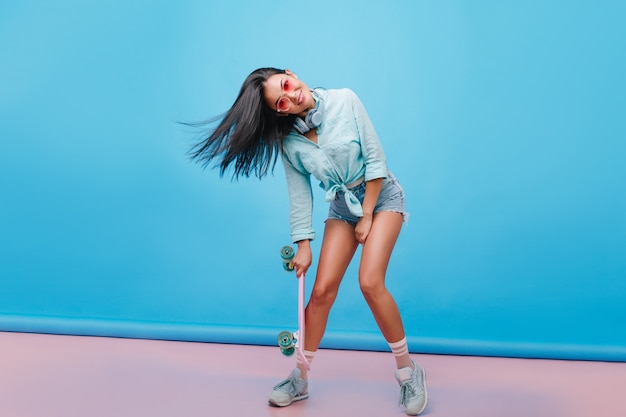 Free photo sensual dark-haired girl in casual street outfit dancing, holding longboard. catching hispanic woman in sneakers  posing with smile.