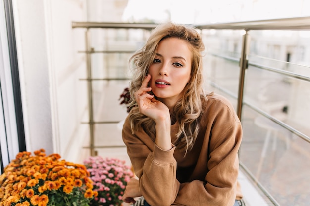 Sensual european girl sitting at terrace. portrait of interested pretty woman posing beside flowers.