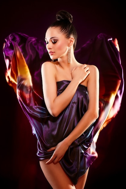 sensual fashion portrait of beautiful sexy brunette girl model posing in bright colorful flying dress, birght makeup isolated in black background