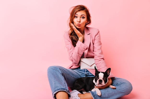 Free Photo sensual ginger lady sitting on the floor with cute french bulldog. jocund trendy woman posing with puppy on pastel.