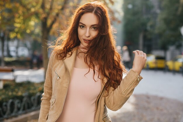 Sensual ginger woman in pink shirt posing on nature wall