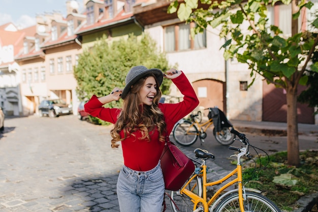 Sensual long-haired girl in red sweater having fun outdoor with bicycle