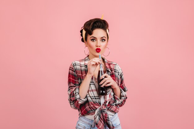 Sensual pinup girl drinking beverage. Studio shot of well-dressed young woman isolated on pink background.