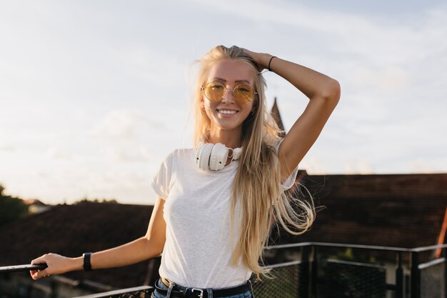 Sensual tanned female model posing on sky background with inspired smile.