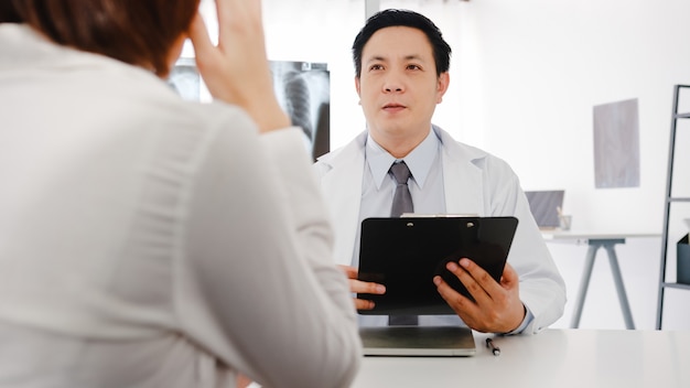 Serious Asia male doctor in white medical uniform using clipboard is delivering great news talk discuss results