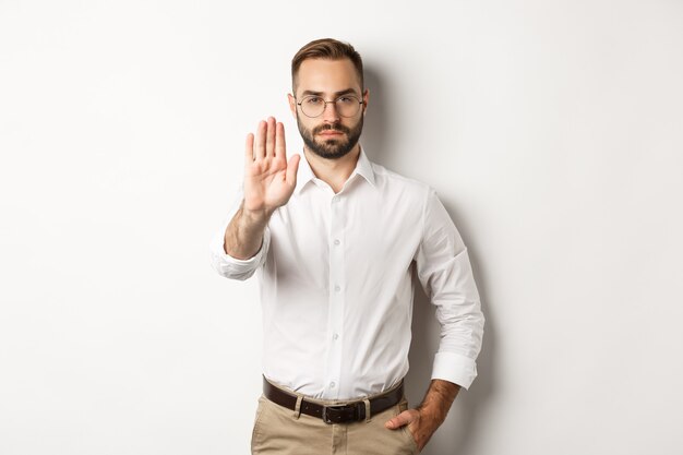 Serious boss in glasses showing stop sign, telling no, forbidding something, standing  white