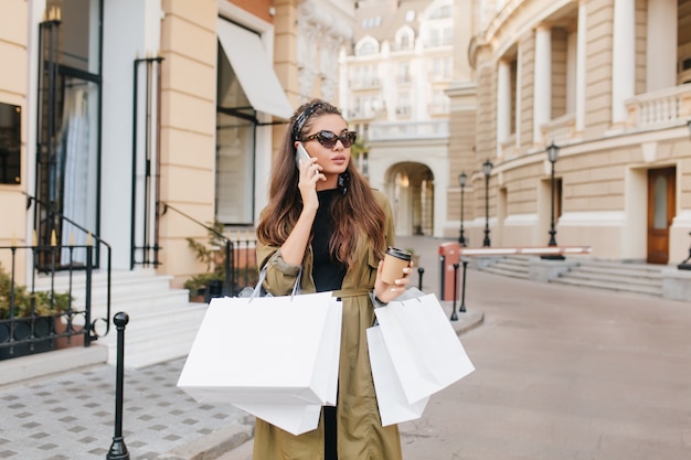 Free photo serious brunette fashionista lady talking on phone during shopping in autumn weekend