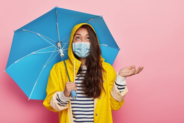 Free photo serious brunette woman raises palm, wears medical mask for protecting herself from virus and catching disease