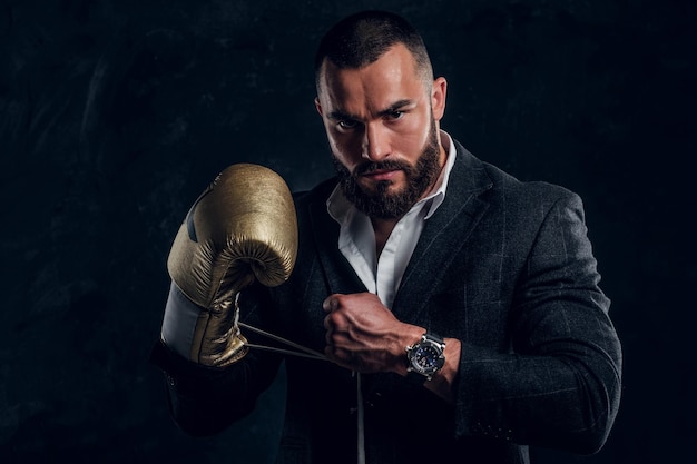 Free photo serious brutal man in suit and golden boxing glove is posing for photographer at dark photo studio.