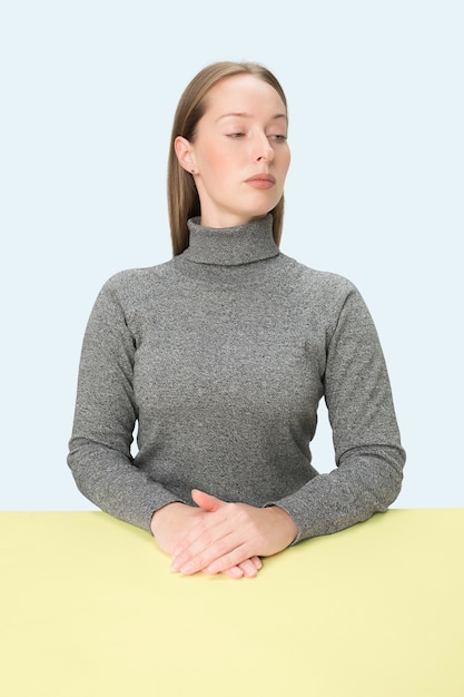 Serious business woman sitting at table on a pink studio background. 