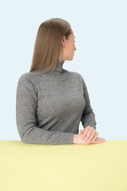 Serious business woman sitting turned away at table on a pink studio background.