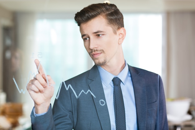 Free photo serious businessman pointing to graph on glass