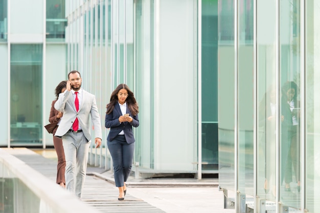 Free Photo serious businesspeople with gadgets going along urban glass wall