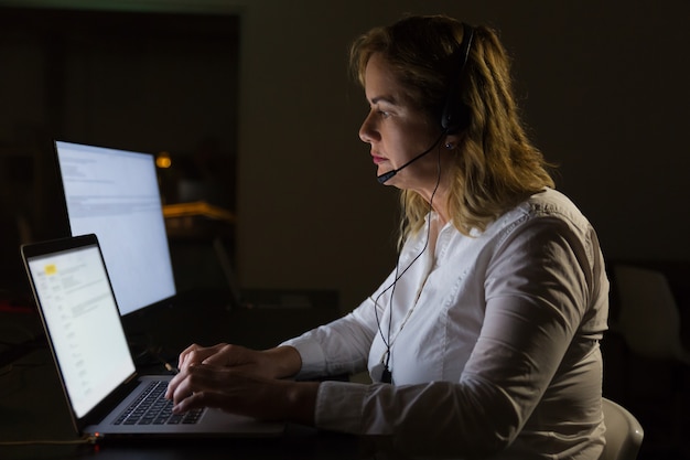 Serious businesswoman in headset typing on laptop