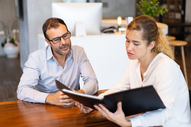 Serious businesswoman showing papers to mid adult executive