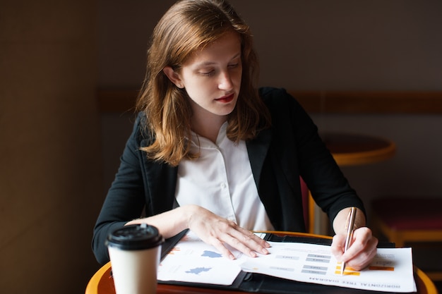 Serious businesswoman working with papers at cafe