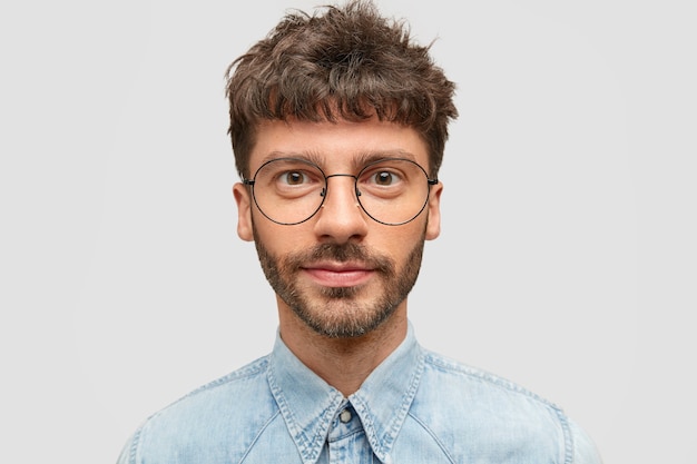 Free photo serious confident unshaven man student in eyewear and denim fashionable shirt, listens information about exam with attention