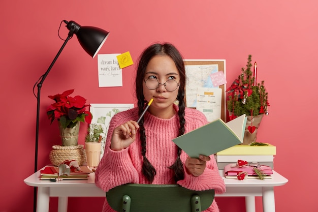 Free Photo serious contemplating asian girl with combed plaits, holds notebook and pencil, writes down future plans and goals for coming christmas