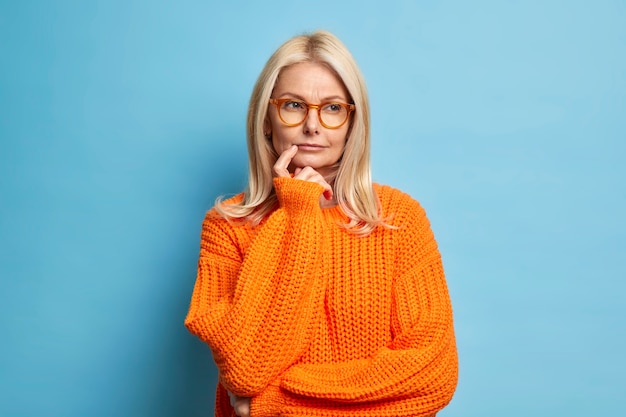 Free photo serious european woman looks thoughtfully considers idea decides on something had doubts dressed in knitted orange jumper.