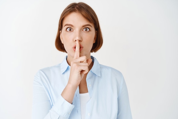 Free Photo serious female office lady shushing, press finger to lips and look concerned, tell to be quiet, make shh gesture, white wall