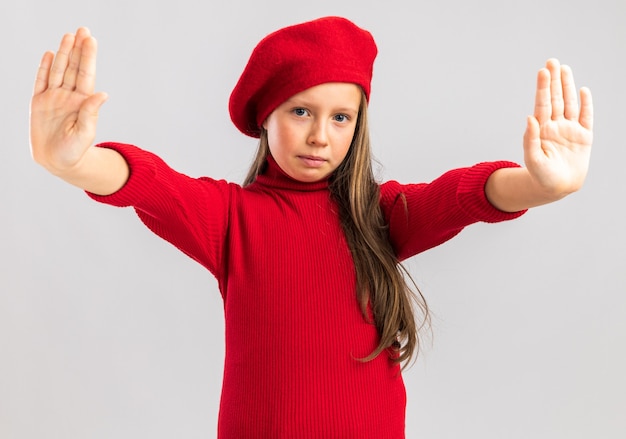 Free Photo serious little blonde girl wearing red beret showing stop gesture looking at front isolated on white wall