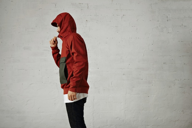 Free photo a serious looking young man zips up his red and grey anorak, portrait from the side isolated on white