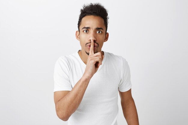 Serious and mad african-american man shushing, press finger to lips, hush gesture