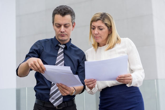 Serious male and female colleagues discussing documents outdoors. 