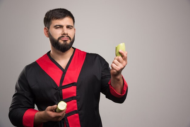 Serious man holding half cut zucchini on grey wall