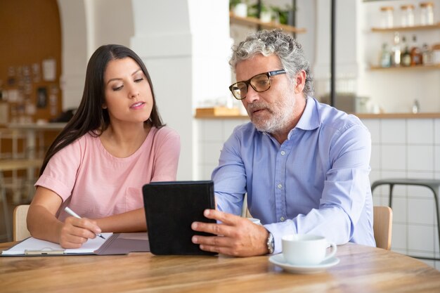 Serious mature male professional showing content on tablet to young colleague